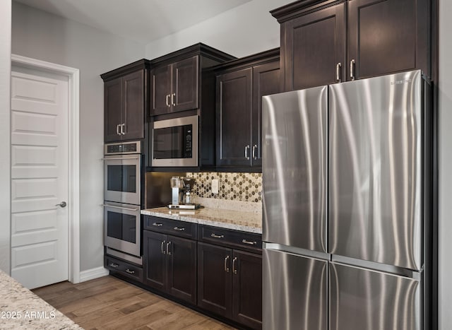 kitchen featuring light stone counters, hardwood / wood-style flooring, dark brown cabinets, and appliances with stainless steel finishes