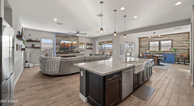 kitchen featuring hanging light fixtures, light wood-type flooring, dishwasher, light stone countertops, and a kitchen island with sink