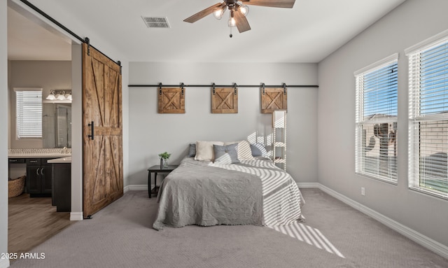 bedroom with ensuite bath, a barn door, ceiling fan, and carpet flooring