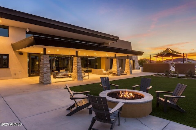 patio terrace at dusk featuring an outdoor fire pit and a yard