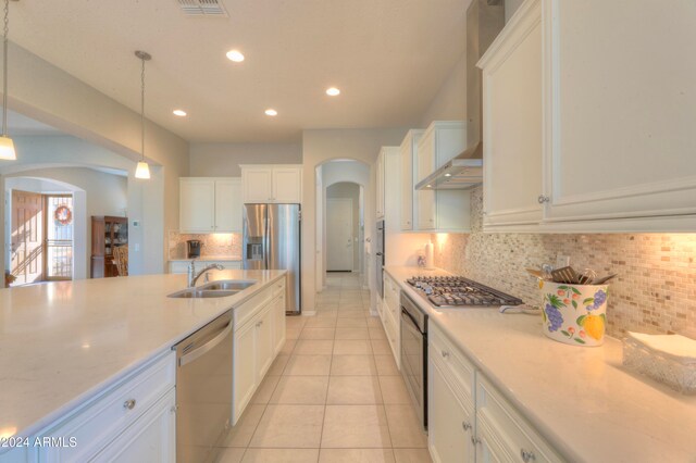 kitchen with wall chimney exhaust hood, sink, hanging light fixtures, stainless steel appliances, and decorative backsplash