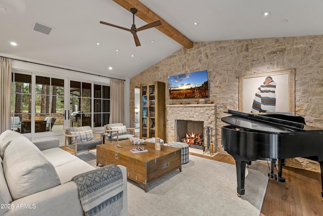 living area featuring lofted ceiling with beams, recessed lighting, wood-type flooring, a ceiling fan, and a stone fireplace