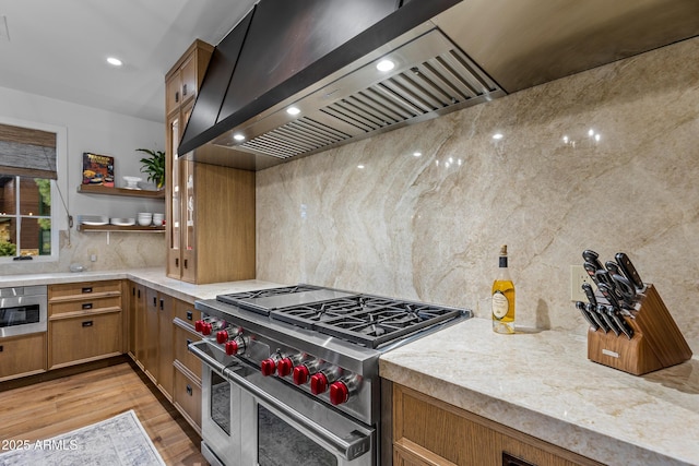 kitchen featuring light wood finished floors, brown cabinets, range with two ovens, backsplash, and premium range hood