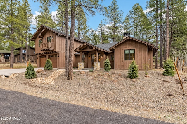 rustic home featuring a balcony, concrete driveway, a garage, a chimney, and board and batten siding