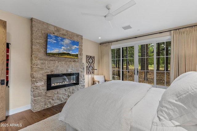 bedroom featuring wood finished floors, a ceiling fan, a fireplace, visible vents, and baseboards