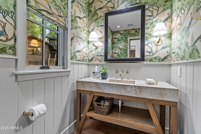 bathroom with wallpapered walls, wainscoting, visible vents, vanity, and wood finished floors