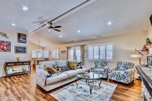 living room featuring ceiling fan with notable chandelier, lofted ceiling with beams, visible vents, and wood finished floors