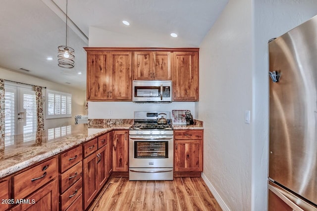 kitchen featuring brown cabinets, light stone counters, stainless steel appliances, and light wood-type flooring