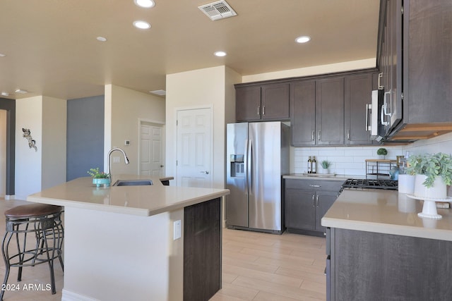 kitchen featuring a kitchen breakfast bar, stainless steel appliances, backsplash, a center island with sink, and sink