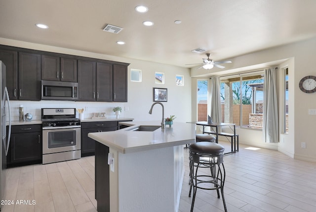 kitchen featuring a kitchen breakfast bar, stainless steel appliances, a center island with sink, sink, and light wood-type flooring