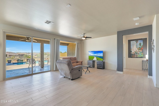 living room featuring ceiling fan, a textured ceiling, and light wood-type flooring