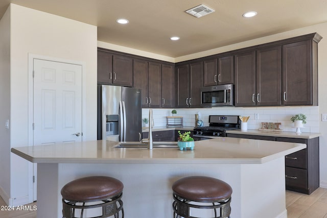 kitchen featuring sink, a kitchen island with sink, stainless steel appliances, and light wood-type flooring