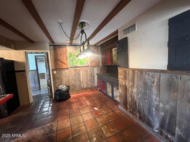 unfurnished dining area featuring beamed ceiling, a textured ceiling, and wood walls