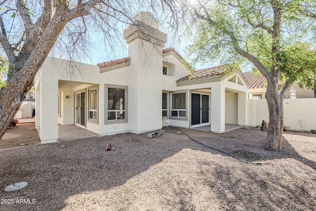 rear view of property featuring stucco siding, a patio, fence, and a tile roof