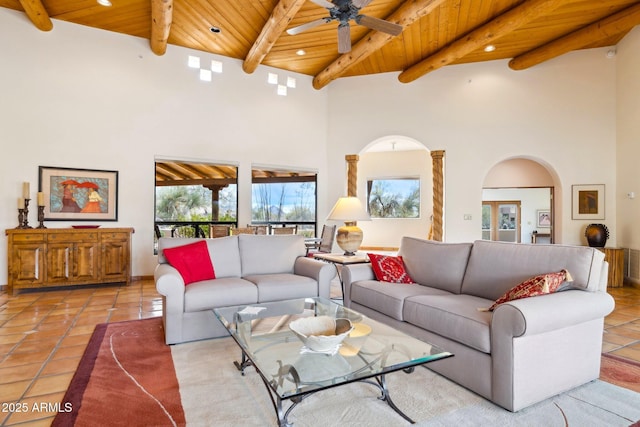 living room with a ceiling fan, light tile patterned flooring, a towering ceiling, wooden ceiling, and beamed ceiling