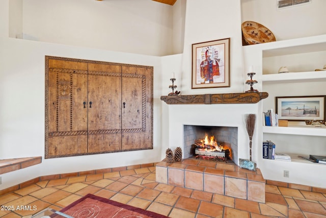 living room featuring visible vents, baseboards, a tiled fireplace, built in features, and a high ceiling