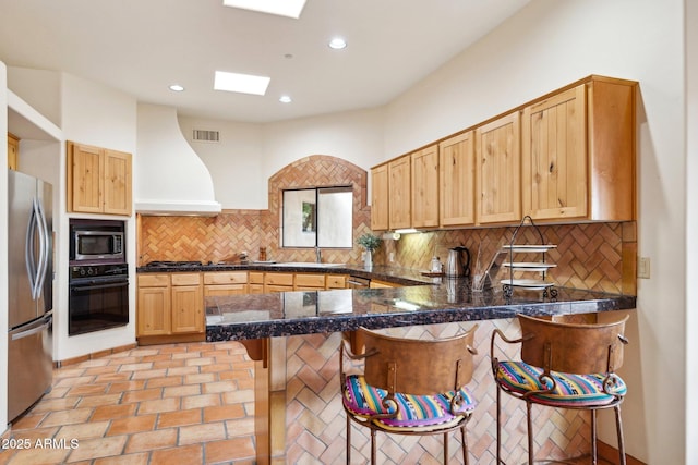 kitchen with a breakfast bar, decorative backsplash, a peninsula, custom exhaust hood, and stainless steel appliances