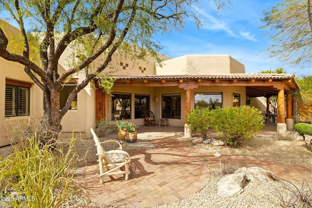 back of property with stucco siding, a tiled roof, and a patio