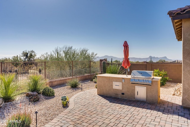 view of patio featuring exterior kitchen, a mountain view, and a grill