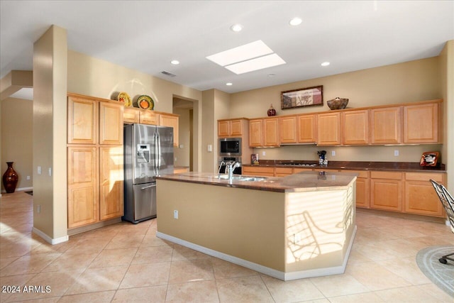 kitchen with light brown cabinets, a skylight, stainless steel appliances, an island with sink, and light tile patterned floors