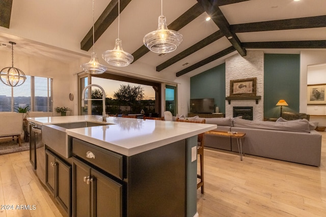 kitchen with light wood-type flooring, a center island with sink, vaulted ceiling with beams, and decorative light fixtures