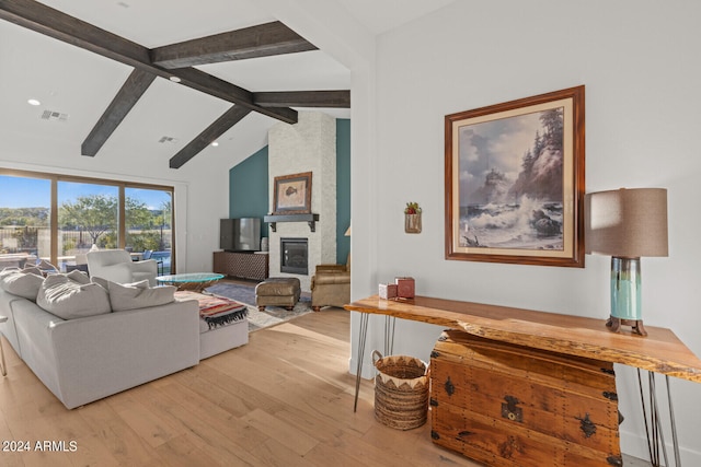 living room featuring vaulted ceiling with beams, light wood-type flooring, and a fireplace