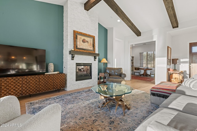 living room with light wood-type flooring, a stone fireplace, beamed ceiling, and high vaulted ceiling