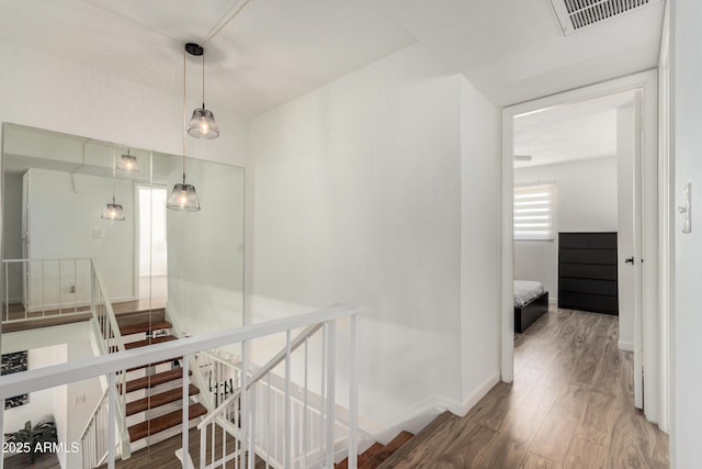 hall with baseboards, an upstairs landing, wood finished floors, and visible vents