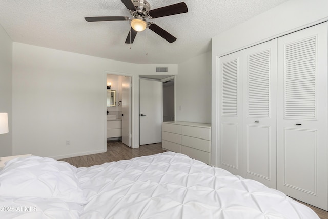 bedroom with a closet, visible vents, wood finished floors, ensuite bathroom, and a textured ceiling