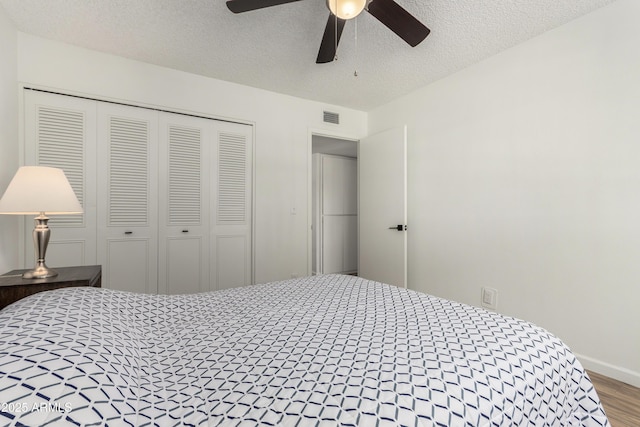 bedroom featuring a textured ceiling, visible vents, wood finished floors, baseboards, and a closet