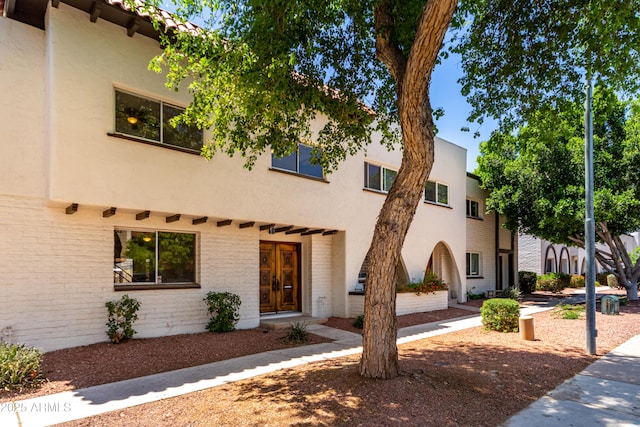 view of front of home featuring brick siding, stucco siding, and french doors