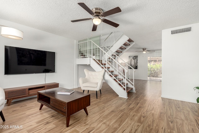 living room with a ceiling fan, stairs, wood finished floors, and visible vents