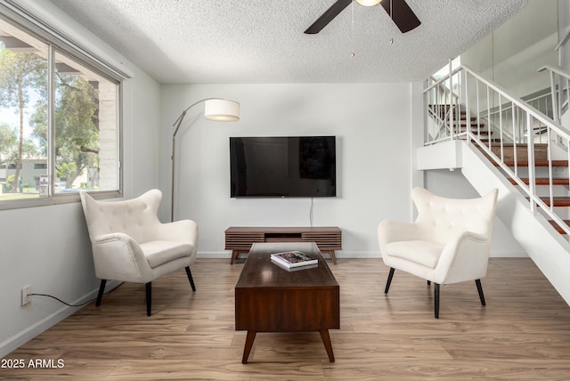 living area with a textured ceiling, ceiling fan, stairway, and wood finished floors