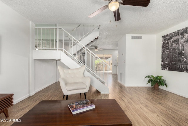 sitting room with a textured ceiling, ceiling fan, visible vents, and stairway