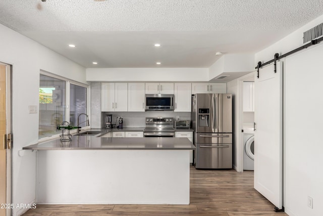 kitchen featuring a peninsula, washer / clothes dryer, white cabinets, a sink, and appliances with stainless steel finishes