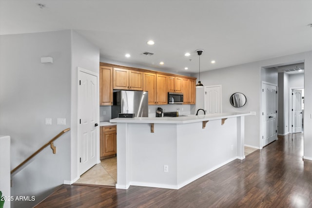 kitchen with a breakfast bar area, hanging light fixtures, light hardwood / wood-style flooring, stainless steel appliances, and a kitchen island with sink