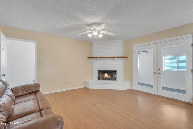 unfurnished living room featuring wood finished floors, ceiling fan, french doors, a textured ceiling, and a brick fireplace