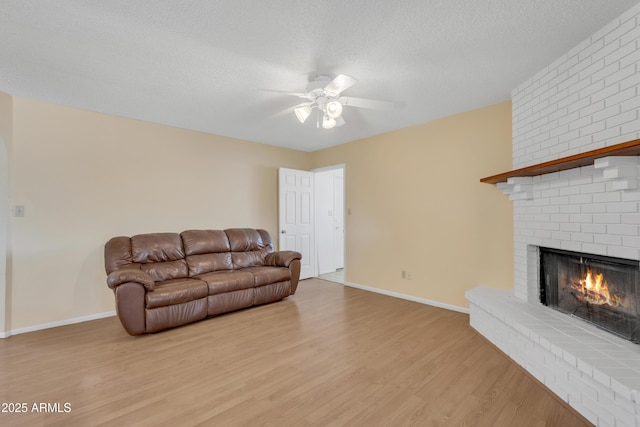 living room with a brick fireplace, a textured ceiling, light wood-style floors, and a ceiling fan