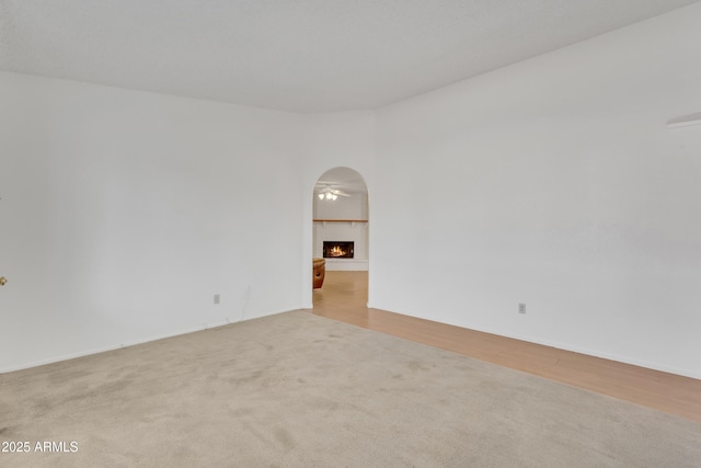 carpeted spare room featuring arched walkways and a brick fireplace