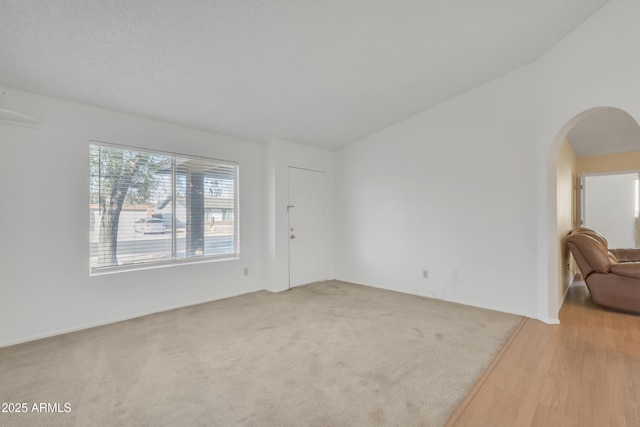 carpeted spare room with arched walkways and lofted ceiling