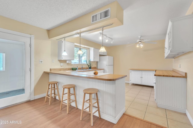 kitchen with visible vents, a peninsula, freestanding refrigerator, a textured ceiling, and white cabinetry