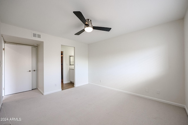 unfurnished bedroom with a closet, light colored carpet, ensuite bath, and ceiling fan