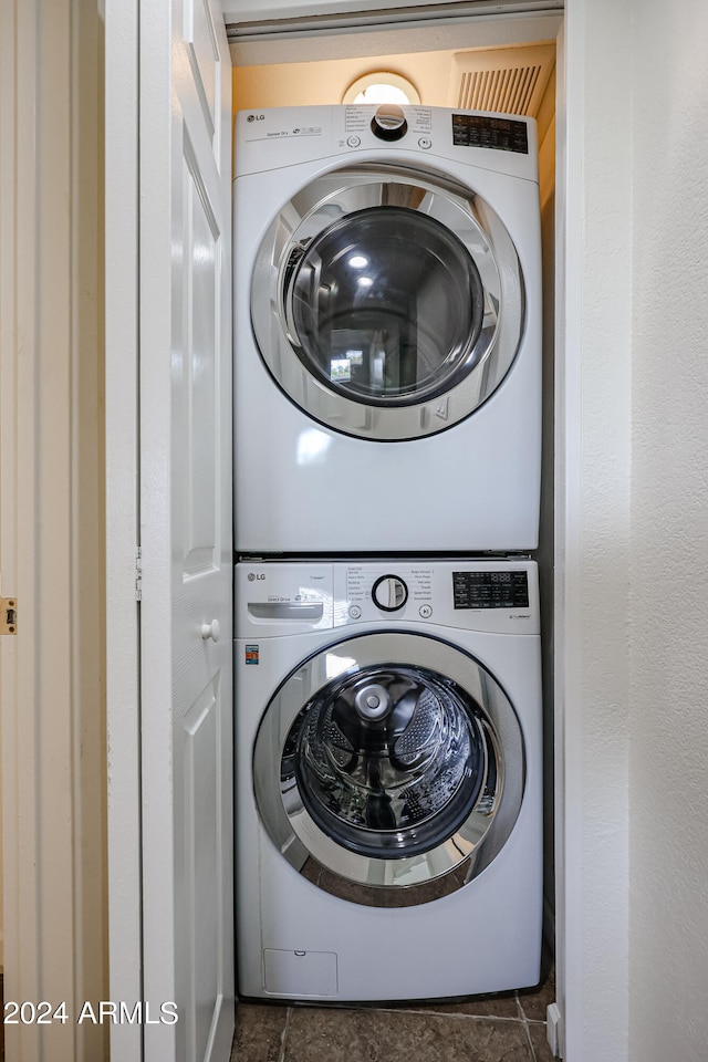 washroom with dark tile patterned flooring and stacked washer and clothes dryer