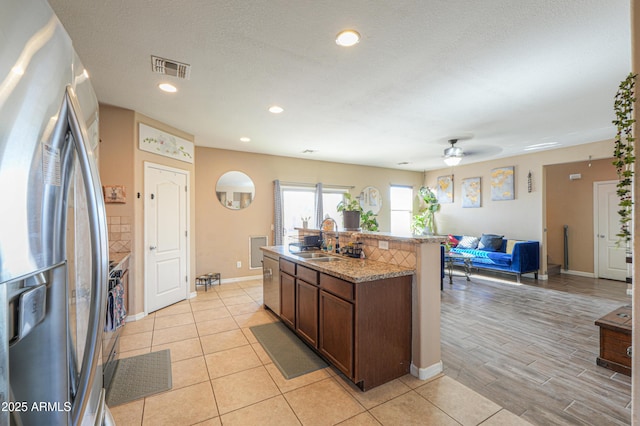 kitchen with a kitchen island with sink, open floor plan, ceiling fan, a sink, and stainless steel appliances