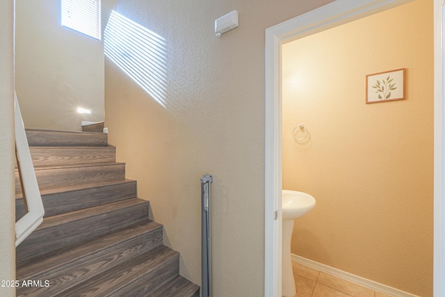 staircase featuring baseboards, a textured wall, and tile patterned flooring