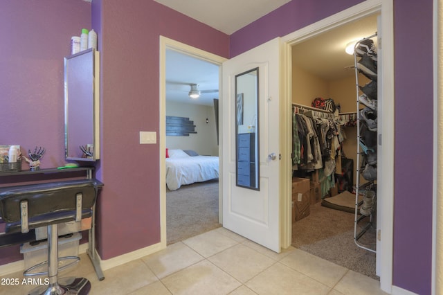 hallway featuring baseboards, light tile patterned flooring, and light carpet