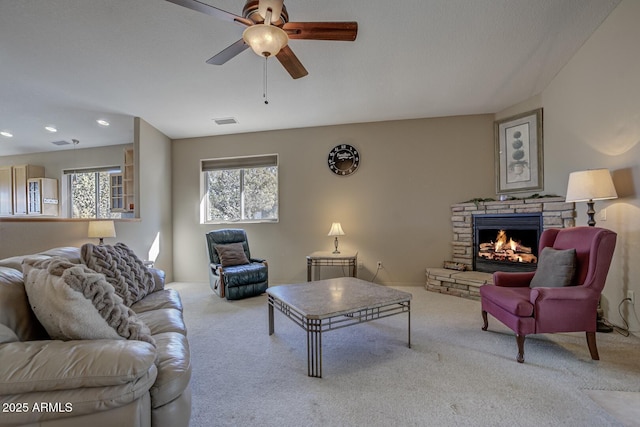 carpeted living room featuring ceiling fan and a stone fireplace