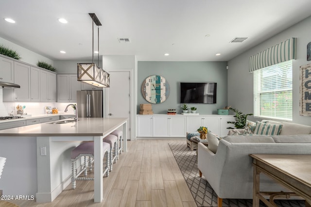 kitchen with a kitchen breakfast bar, hanging light fixtures, stainless steel appliances, sink, and white cabinetry