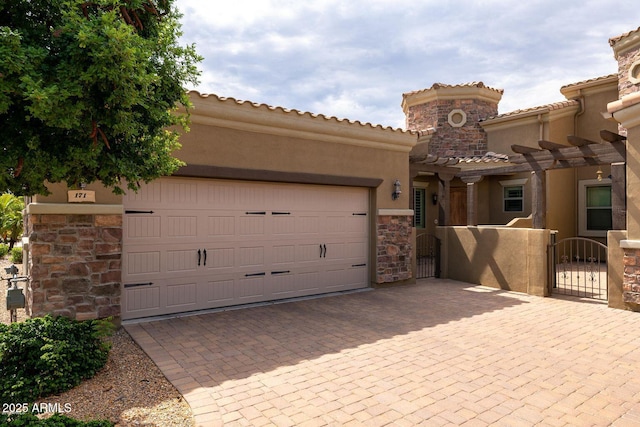 mediterranean / spanish-style home with stone siding, an attached garage, a gate, decorative driveway, and stucco siding