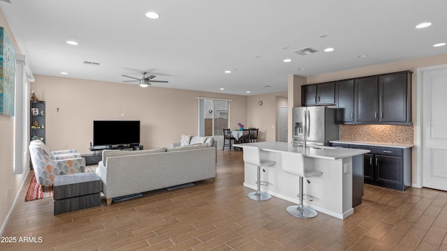 kitchen with visible vents, a kitchen bar, stainless steel refrigerator with ice dispenser, wood finished floors, and light countertops